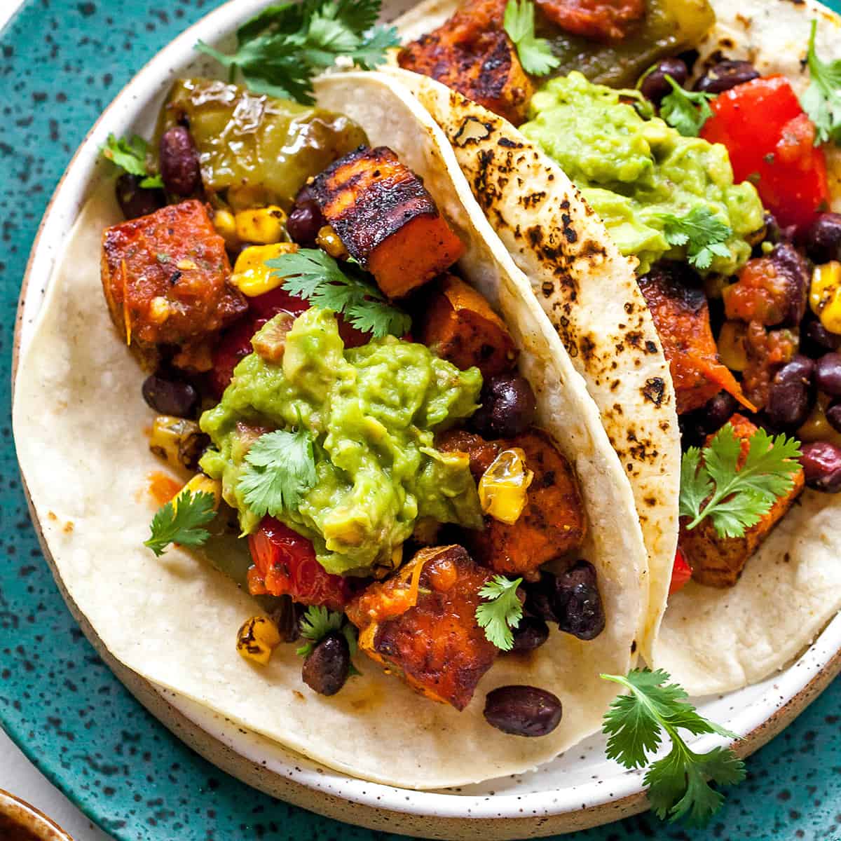two black bean sweet potato tacos on a plate with guacamole and cilantro