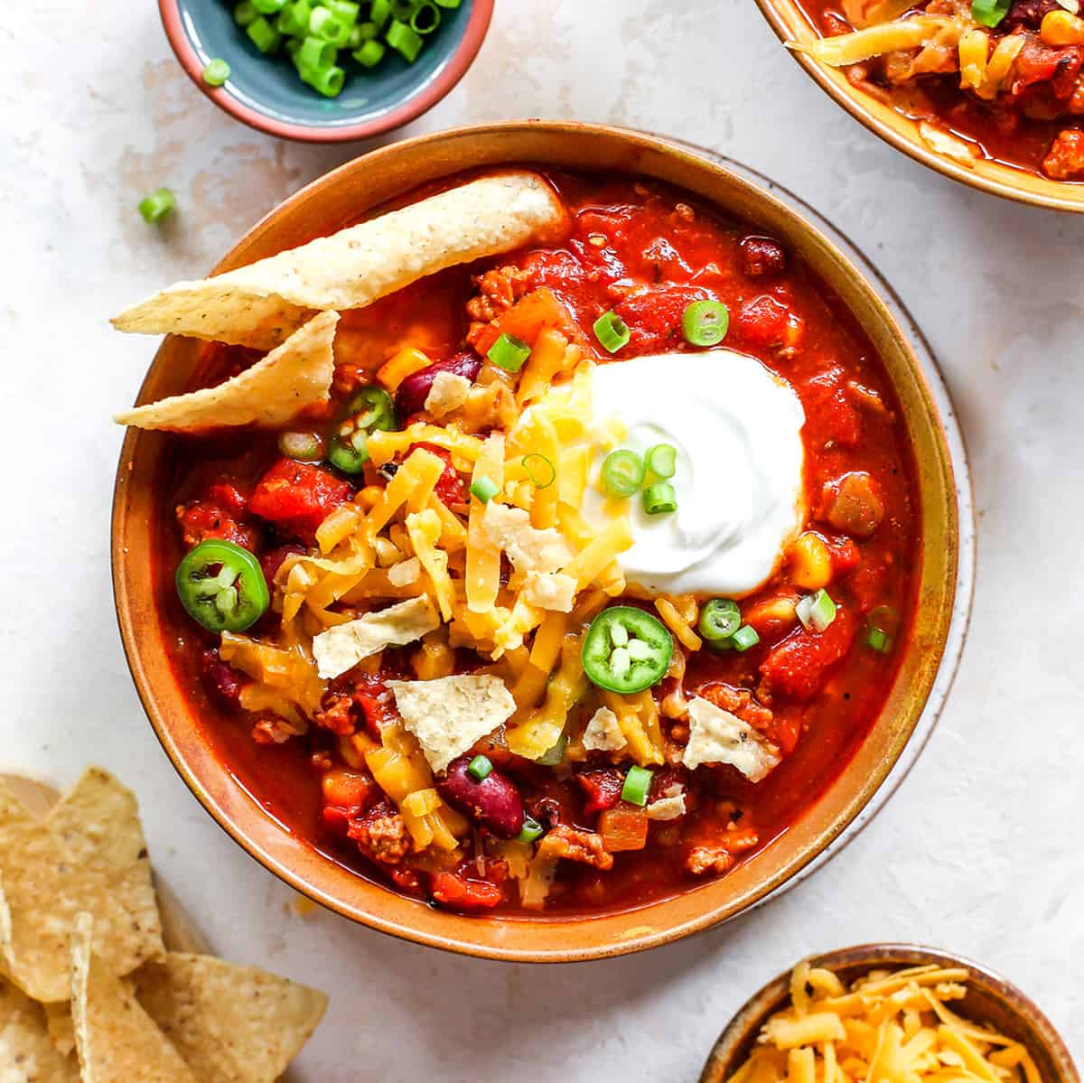 overhead photo of a bowl of turkey chili with sour cream, cheese, chips and green onions 