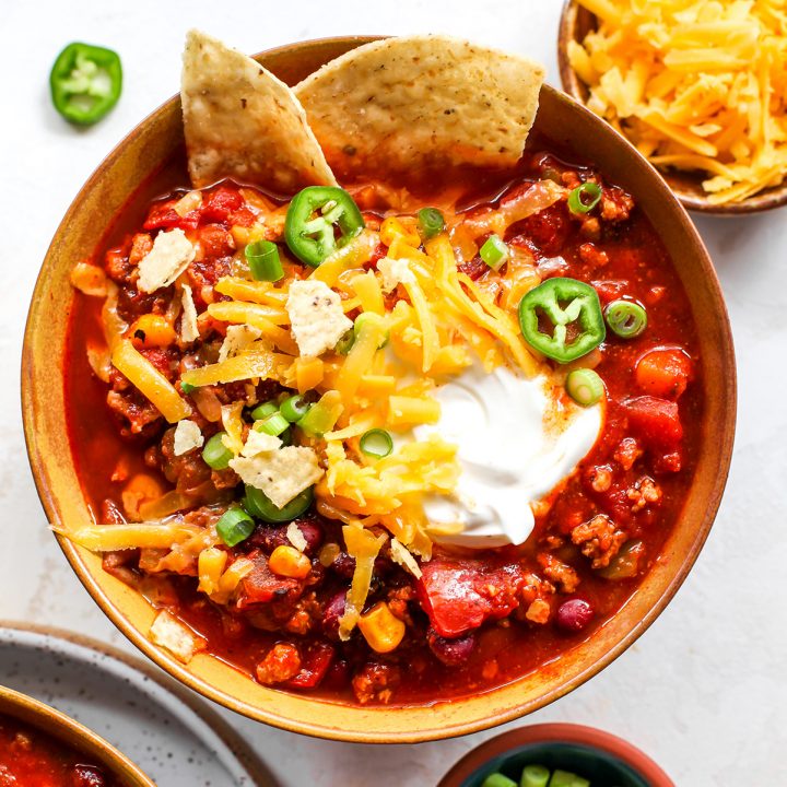overhead view of a bowl of turkey chili with sour cream, cheese, chips and green onions