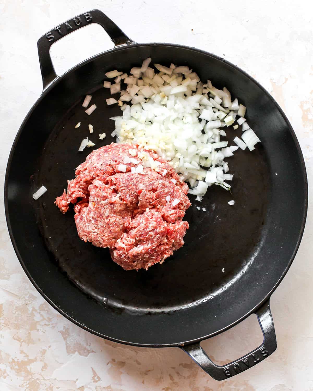 making sausage cream cheese dip - raw breakfast sausage, minced garlic and diced onion in a black cast iron skillet before cooking