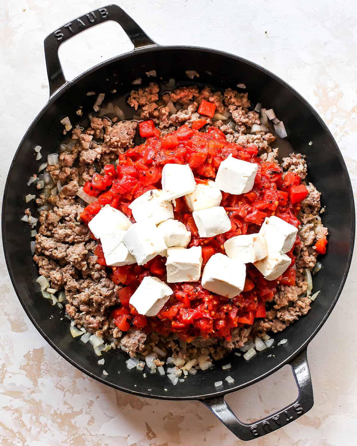 making sausage cream cheese dip - cooked ground beef and onion mixture in a black skillet with diced tomatoes and green chiles added as well as diced cream cheese before sitrring