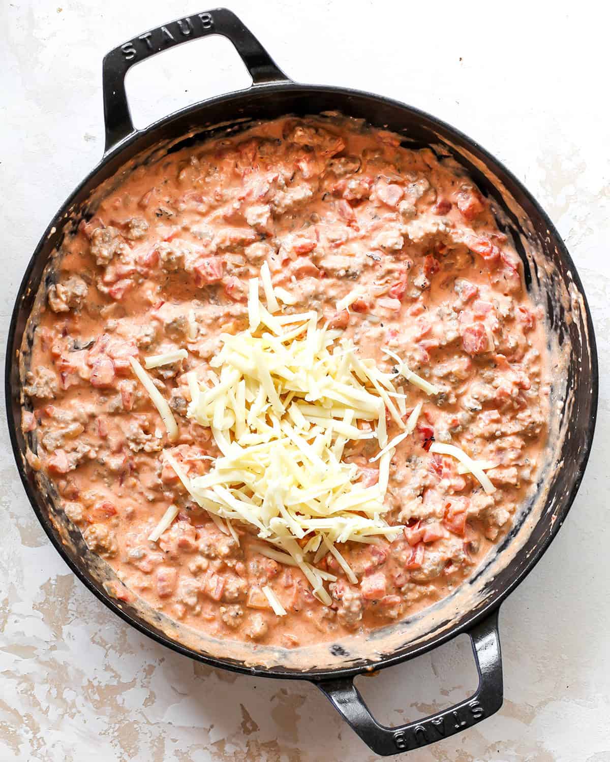 making sausage cream cheese dip - cheddar cheese added to the dip in a black cast iron skillet before mixing