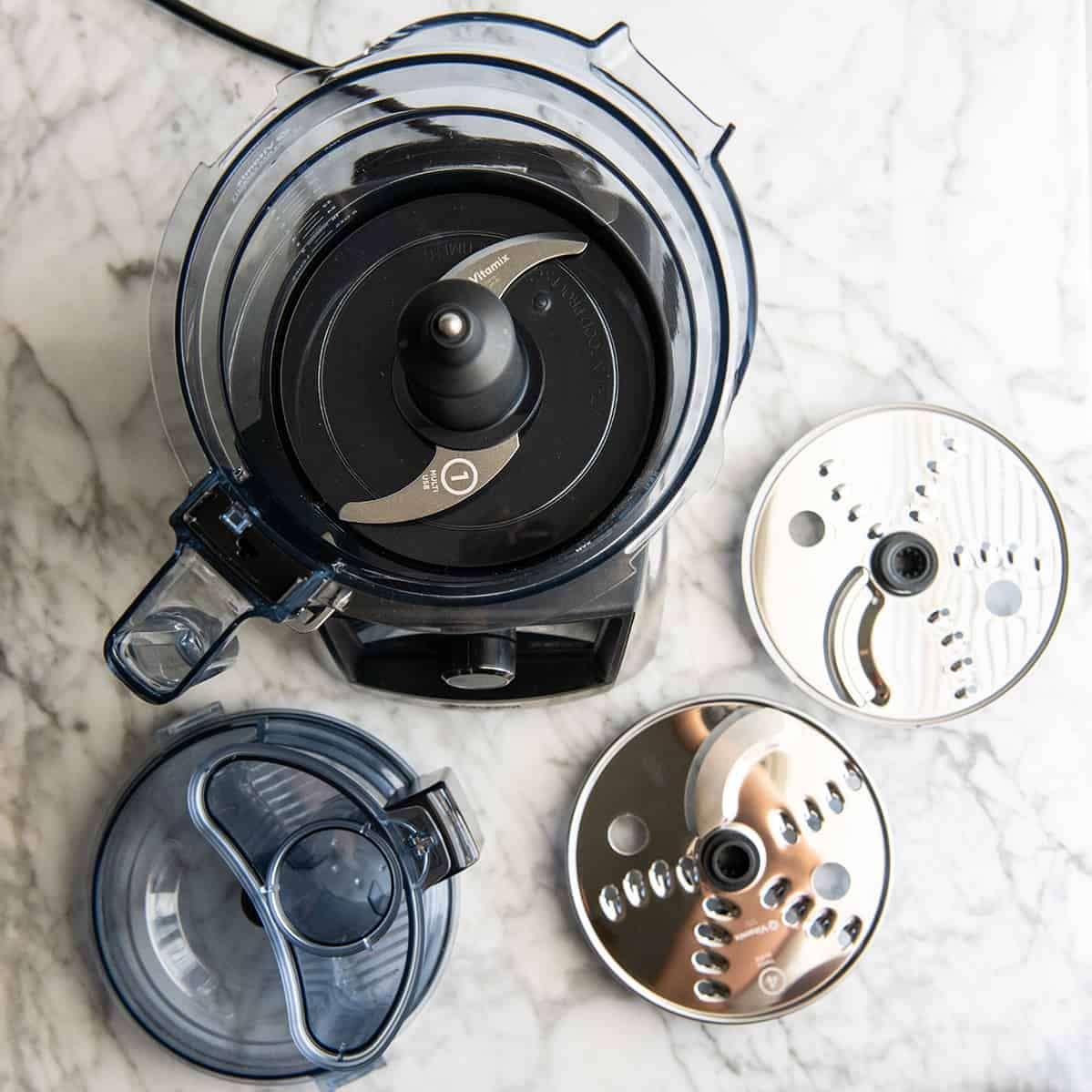 Overhead view of the Vitamix food processor with the multi-use blade attached and the other discs around it