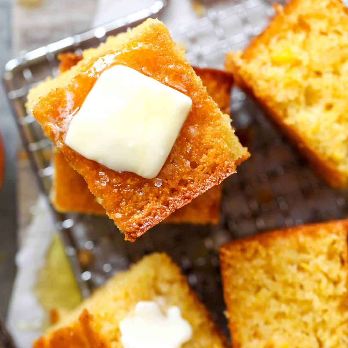 overhead photo of 5 pieces of cornbread, two are stacked on top of each other with melting butter and honey on top. the other 3 are laying on a wire rack on their side so the moist texture is visiable. 