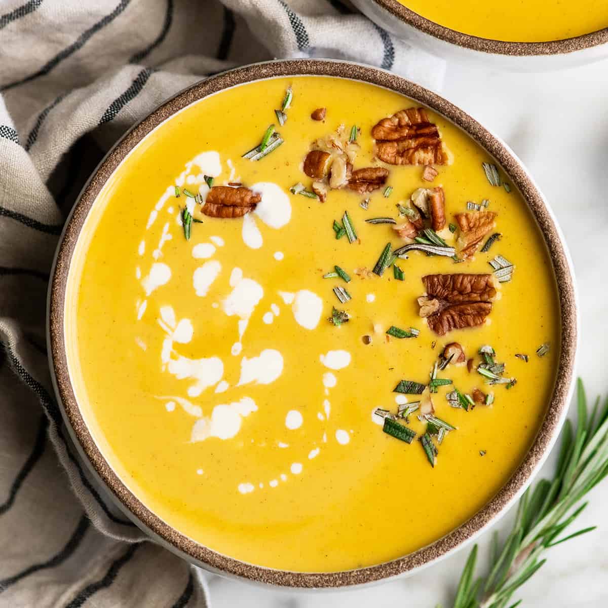 Overhead view of a bowl of butternut squash soup with cream, herbs and nuts 