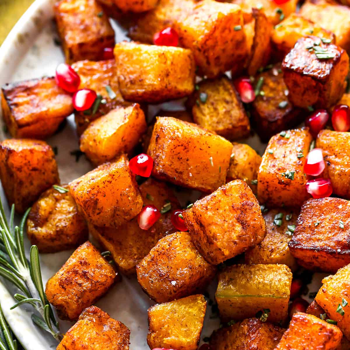 up close overhead view of Cinnamon Roasted Butternut Squash on a plate with pomegranates and rosemary