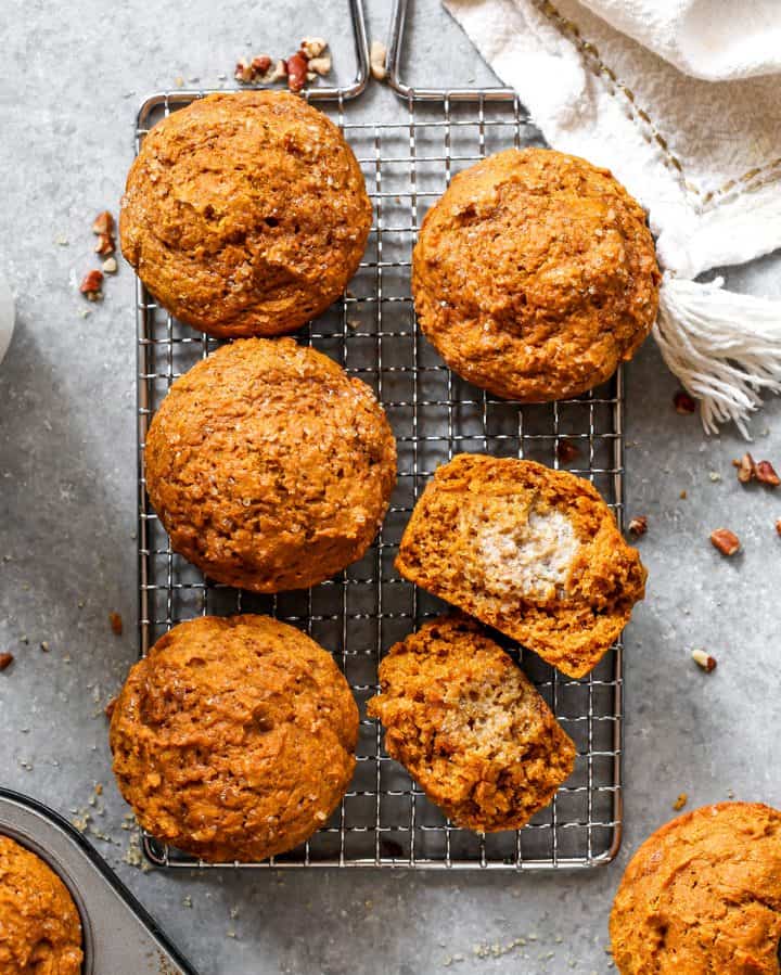 visualizzazione di 4 Healthy Pumpkin Muffin su una griglia di raffreddamento, uno tagliato a metà.