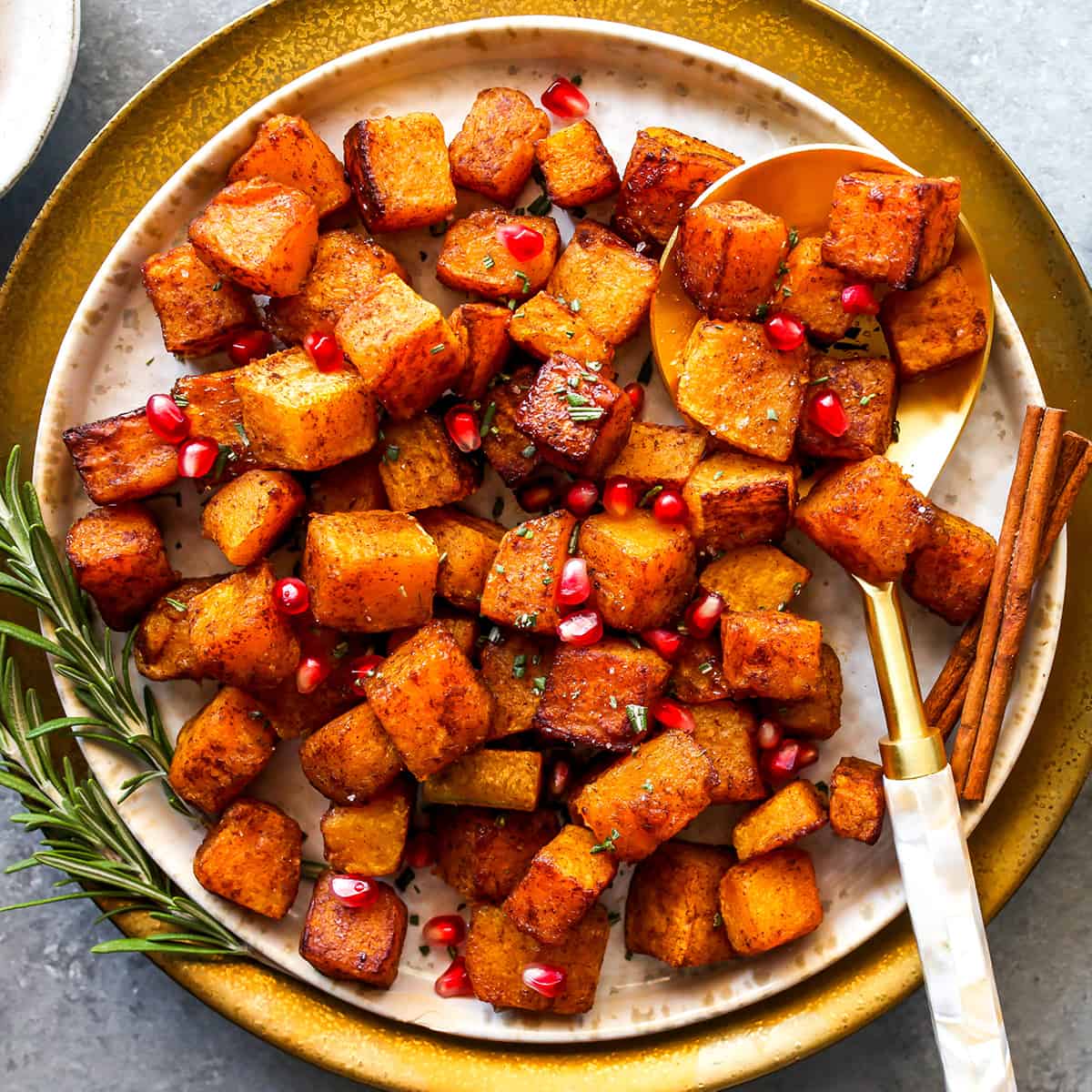 overhead view of cinnamon roasted butternut squash on a plate with pomegranates and rosemary