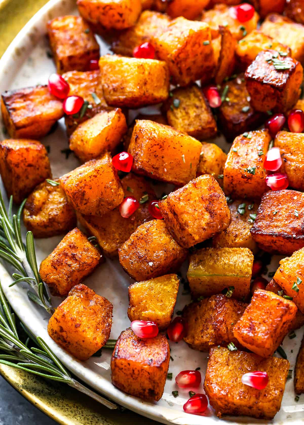 up close overhead view of Cinnamon Roasted Butternut Squash on a plate with pomegranates and rosemary