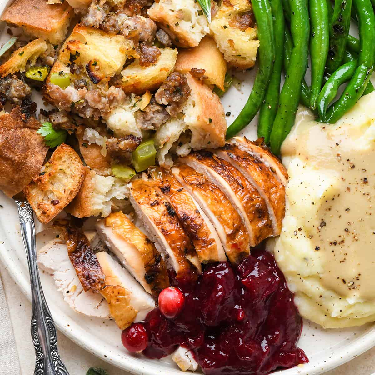 thanksgiving recipes on a plate - turkey, stuffing, green beans, mashed potatoes, gravy and cranberry sauce. 