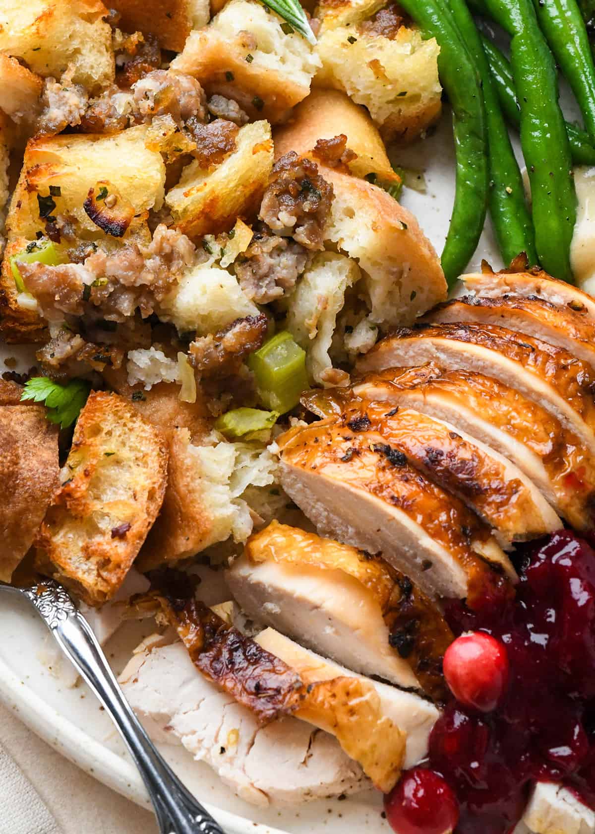 thanksgiving recipes on a plate - turkey, stuffing, green beans, mashed potatoes, gravy and cranberry sauce. 