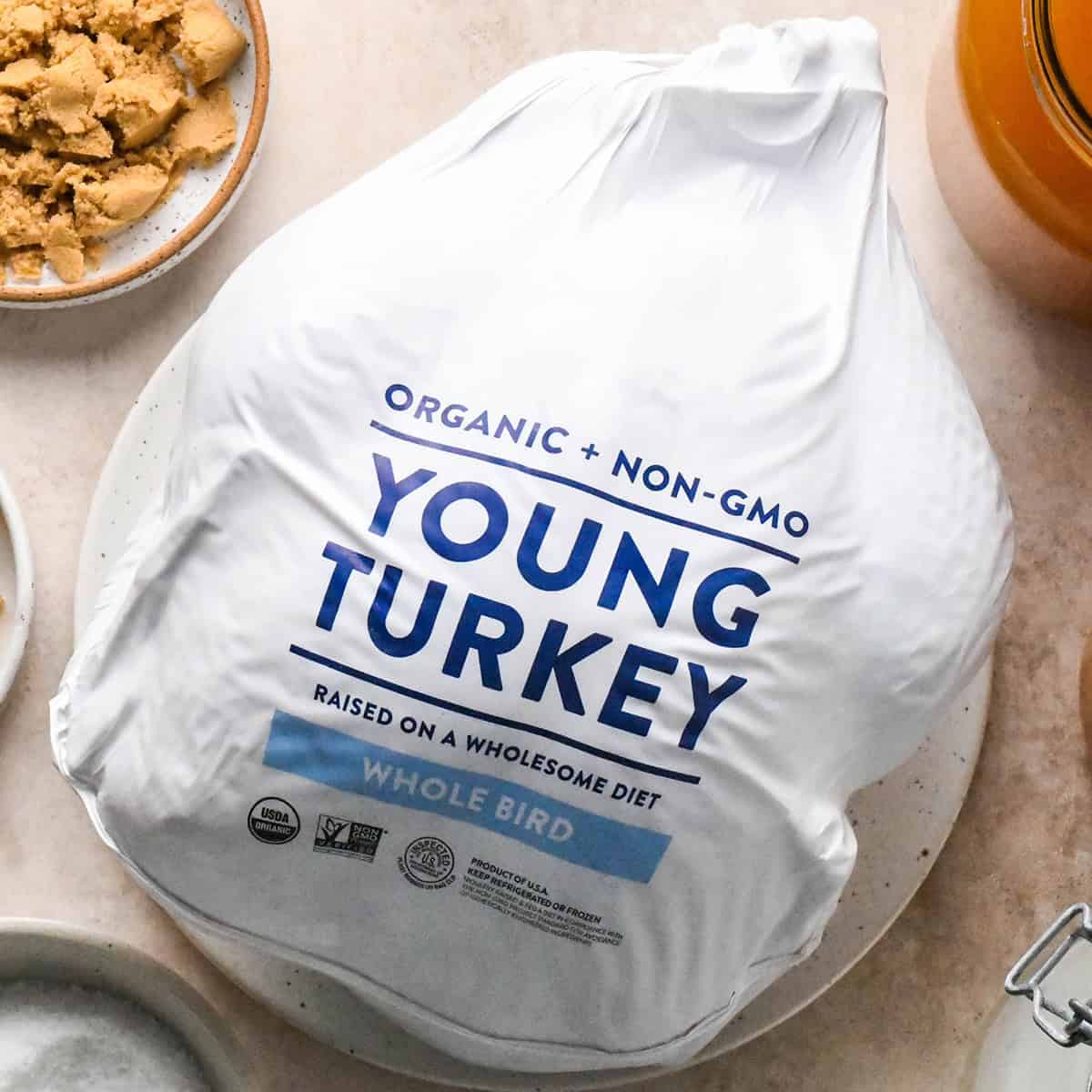 How to Roast a Turkey - a full turkey in the package set out to thaw on a counter with other ingredients around it 