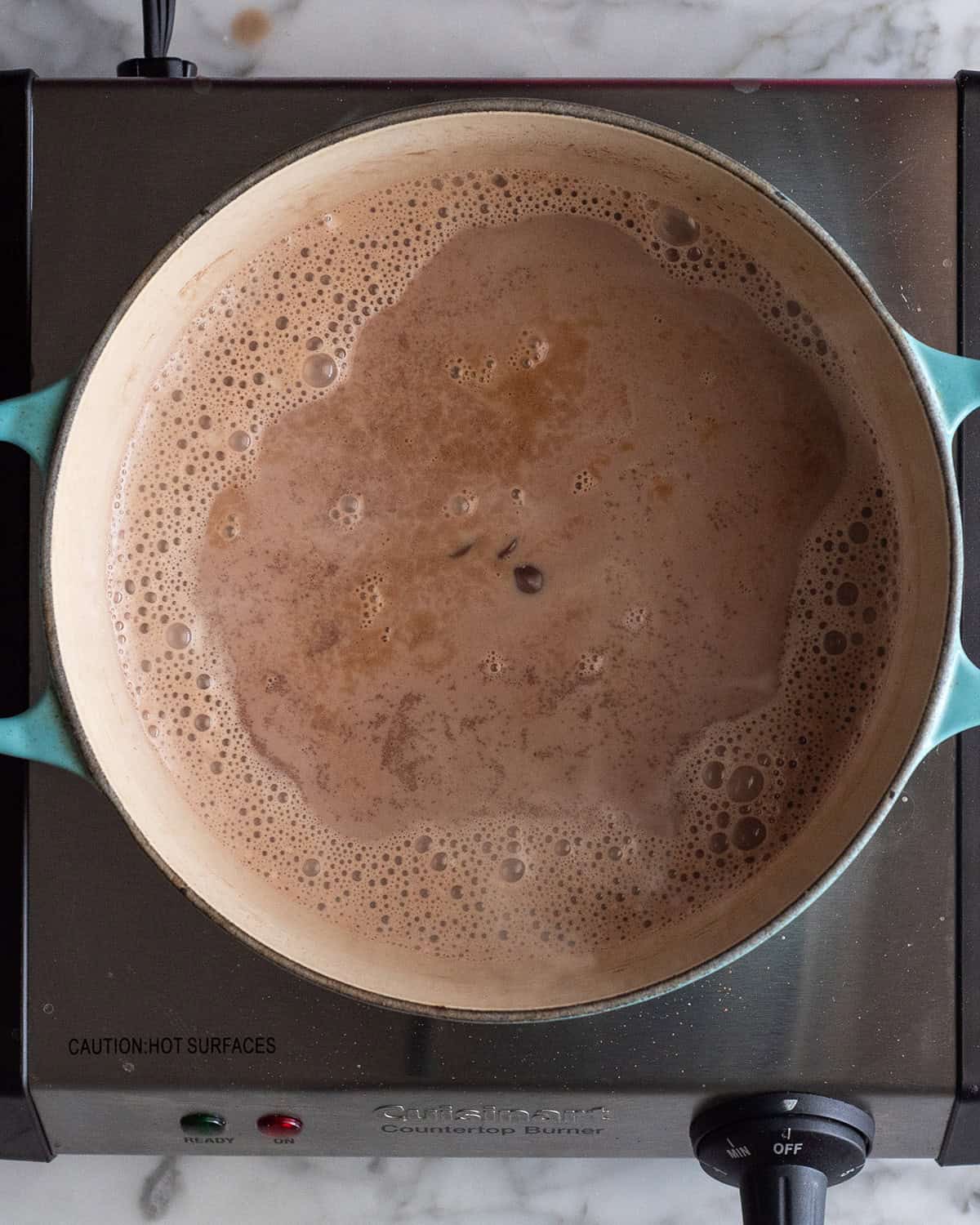 making homemade hot chocolate recipe - semisweet chocolate and vanilla added to the mixture in a blue dutch oven on an electric cook top before mixing