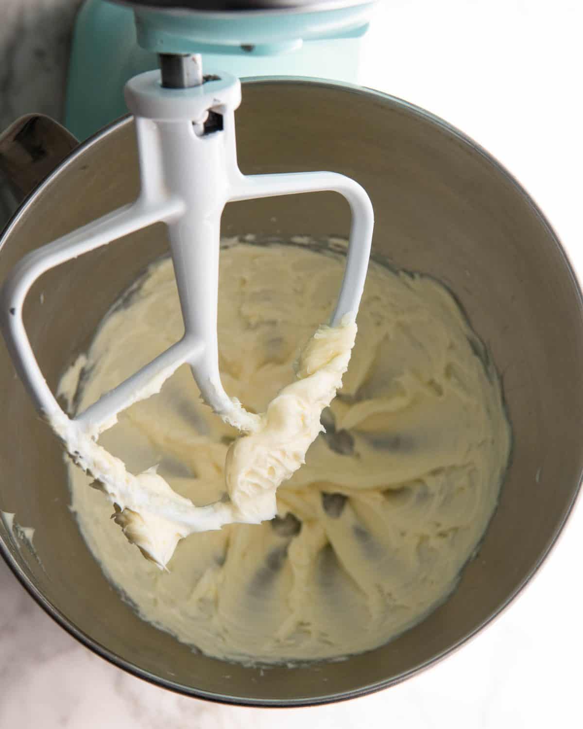 making pecan snowball cookies recipe - butter beaten in a light blue kitchen aid fitted with a metal mixing bowl and white paddle attachment
