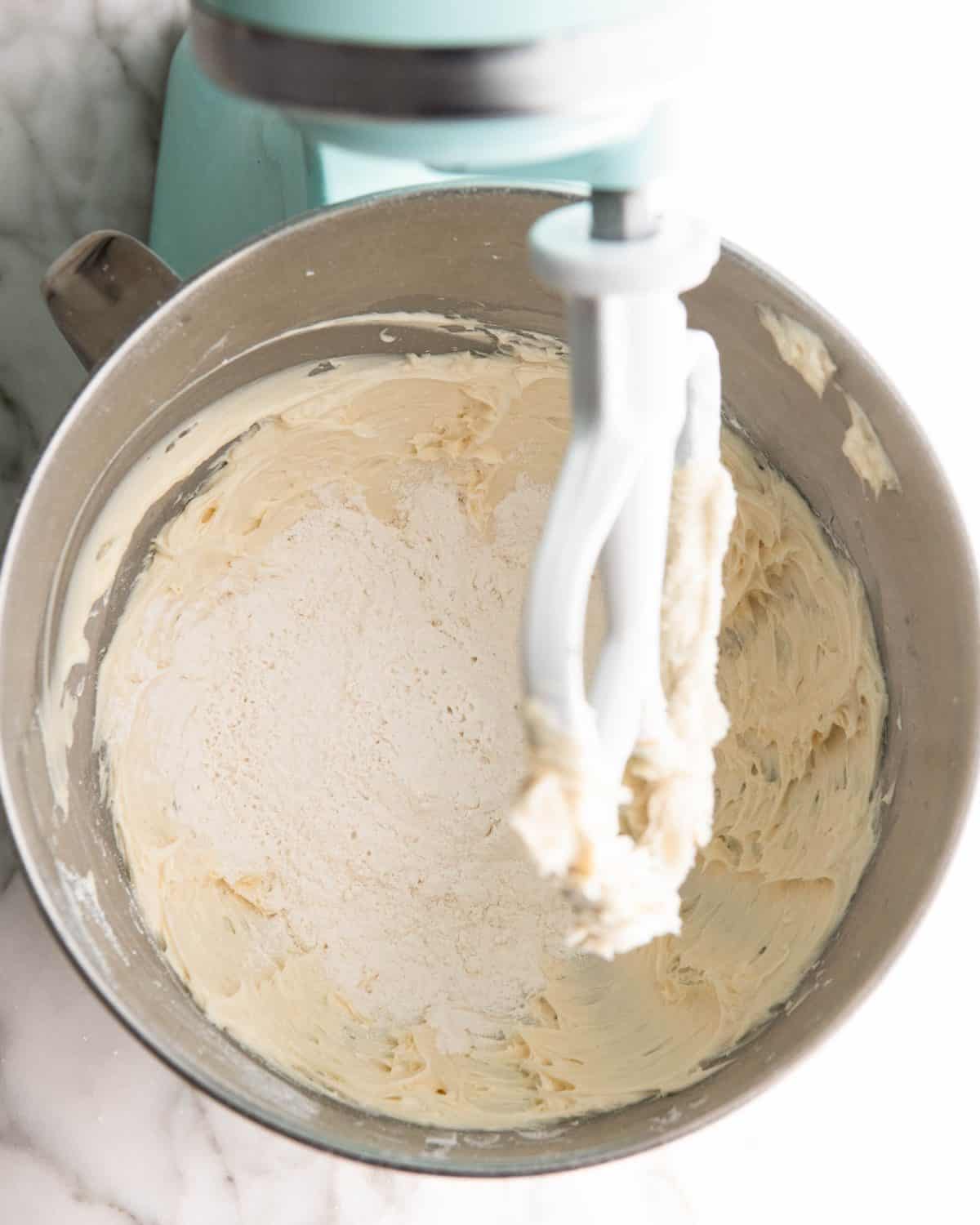 making pecan snowball cookies recipe - flour and salt added to the dough before mixing in a light blue kitchen aid fitted with a metal mixing bowl and white paddle attachment