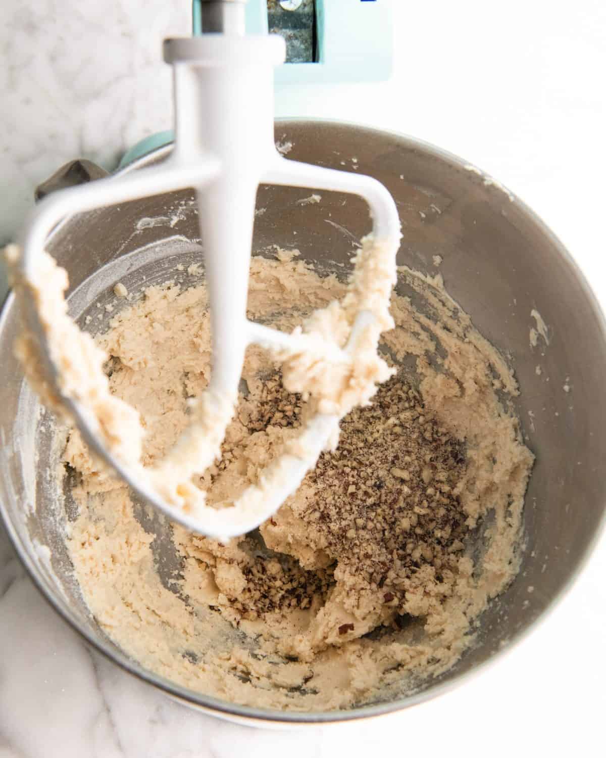 making pecan snowball cookies recipe - pecans added to the dough before mixing in a light blue kitchen aid fitted with a metal mixing bowl and white paddle attachment