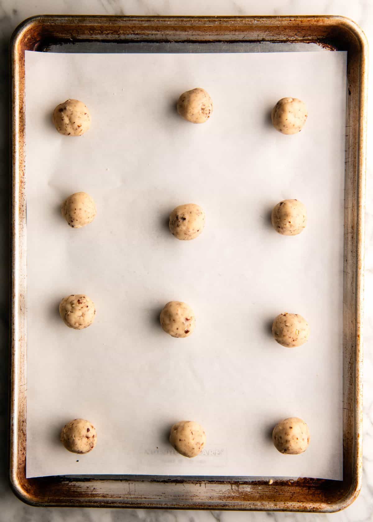 12 pecan snowball cookies dough balls on a parchment-lined metal baking sheet before baking