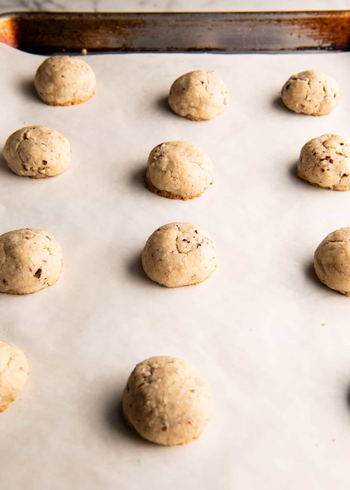 12 pecan snowball cookies on a metal baking sheet lined with white parchment paper after baking