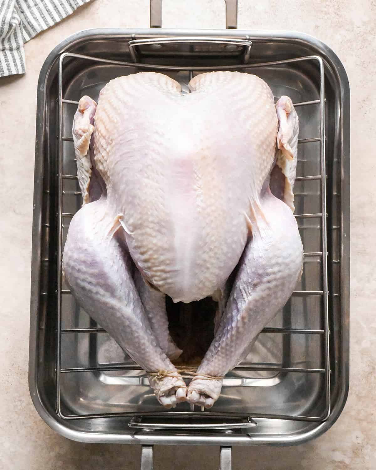 a raw whole turkey on a wire rack on a roasting pan after brining to make oven roasted turkey