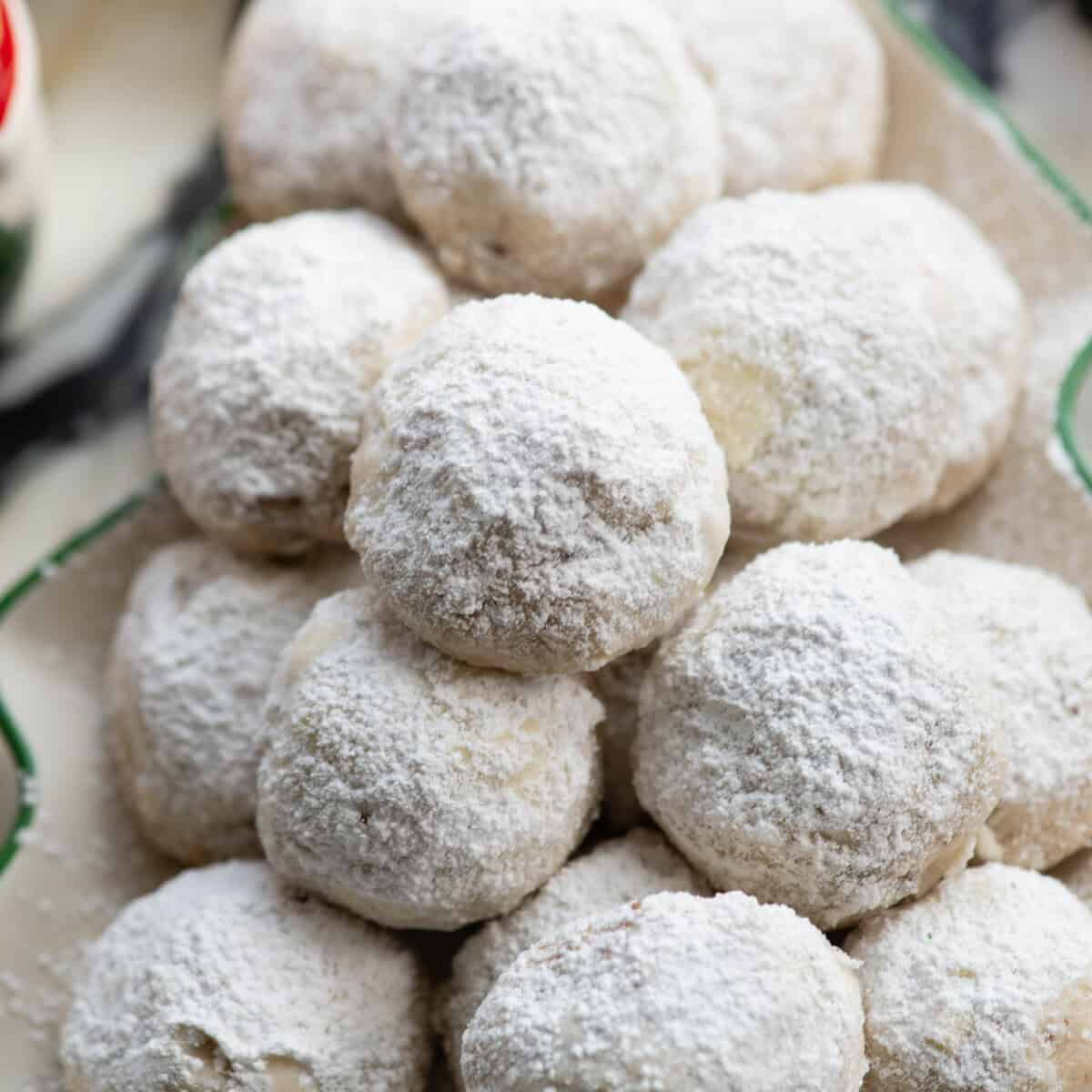 Pecan Snowball Cookies are easy to make with 7 ingredients. They are buttery, nutty, and melt-in your mouth delicious. These butterball cookies are an old family recipe, and a must-make Christmas cookie! close up photo of snowball cookies piled on a Christmas tree shaped plate
