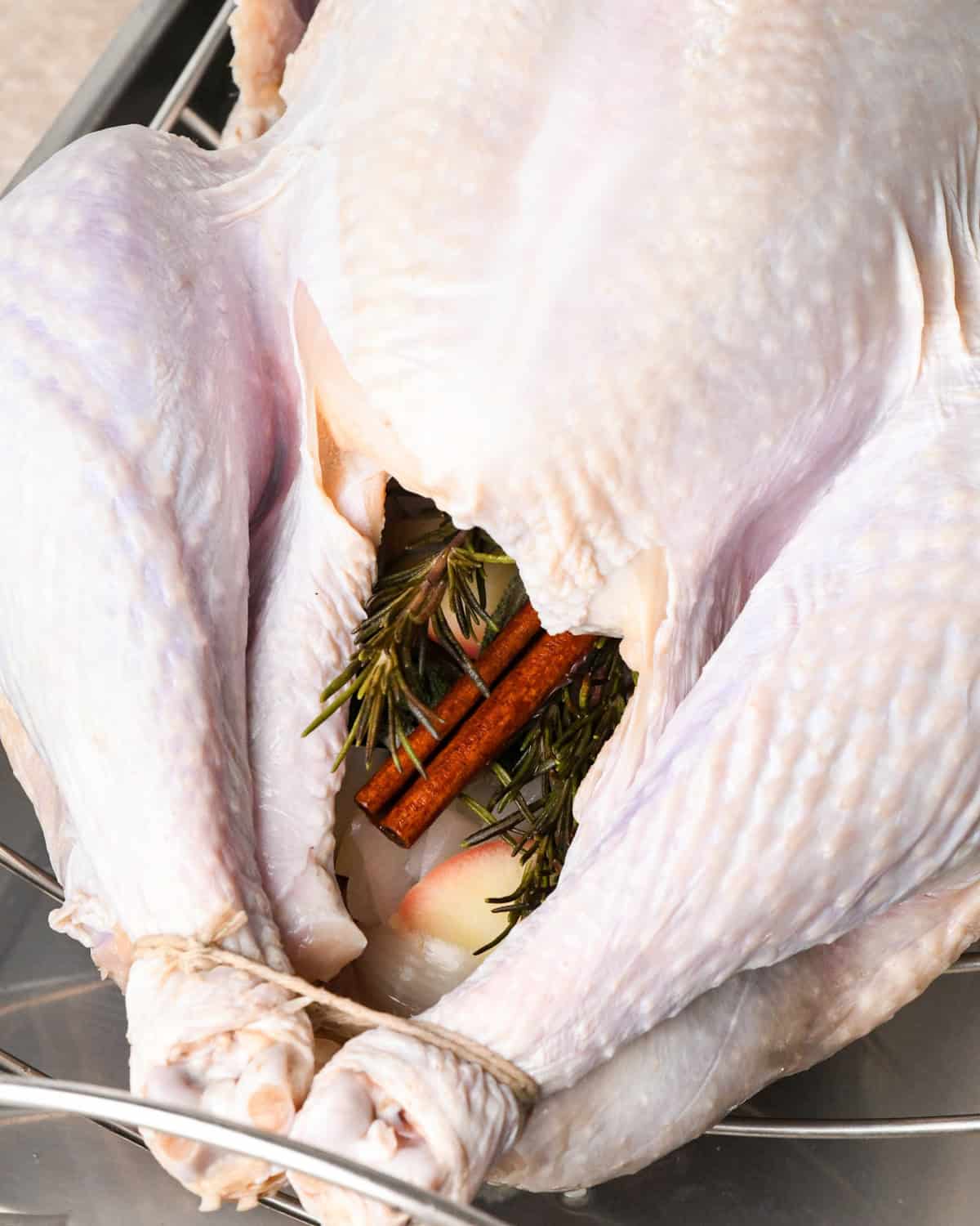 aromatics in the cavity of a whole, uncooked turkey on a wire rack in a roasting pan