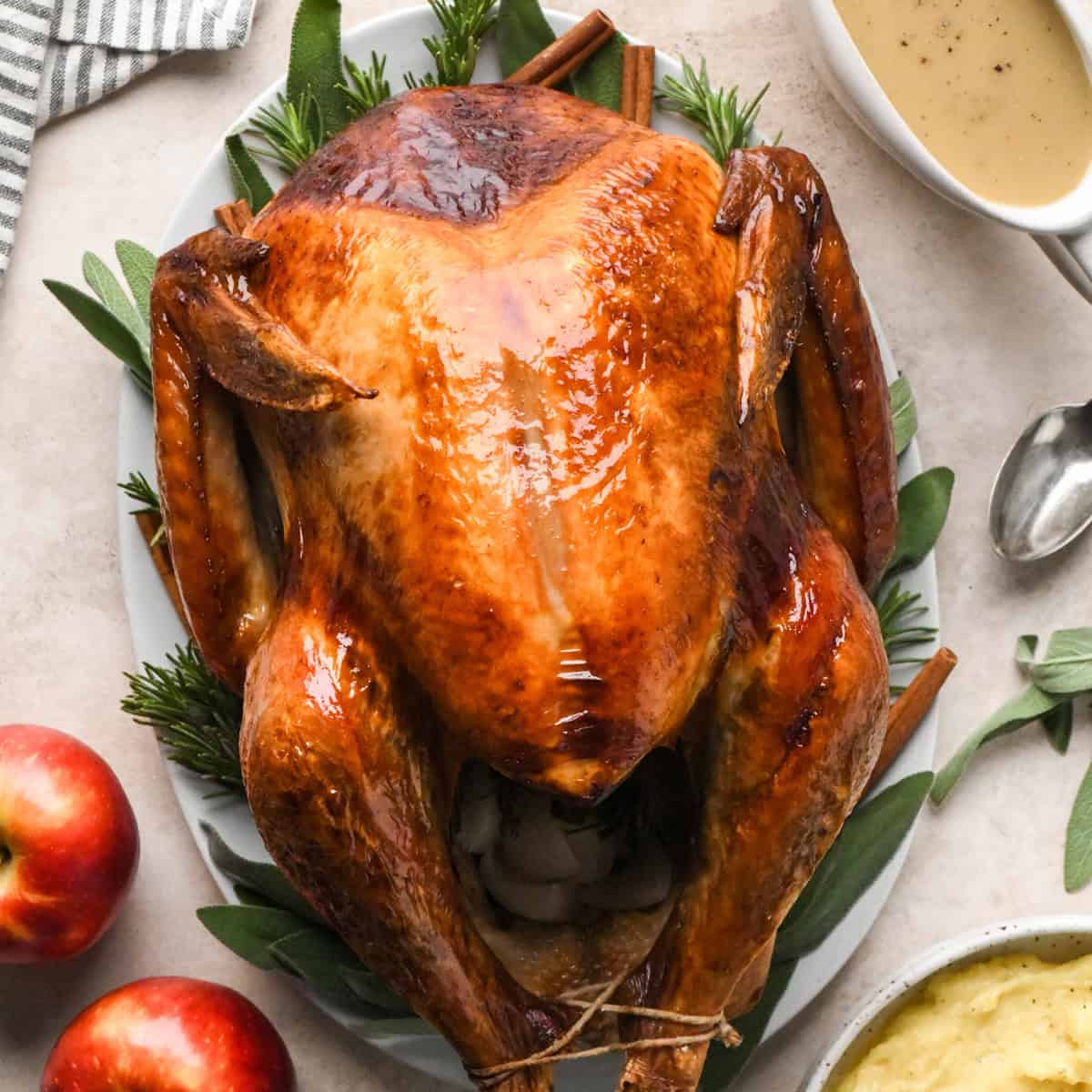 Oven Roasted Turkey on a serving plate with herbs, apples, gravy and cinnamon sticks