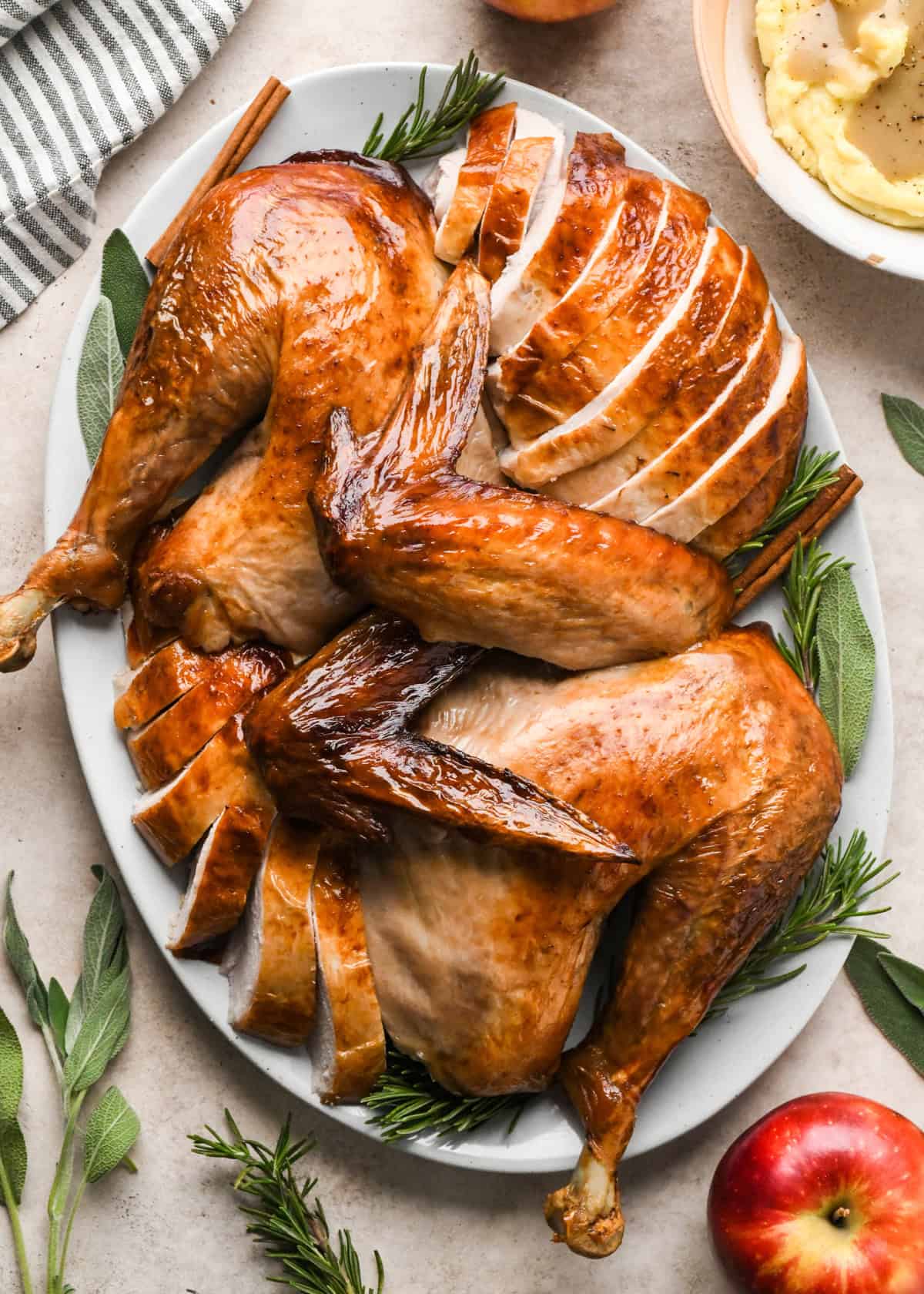 pieces of a roast turkey on a plate after carving - wings, thighs, sliced breast, with the skin on and herbs around it. 