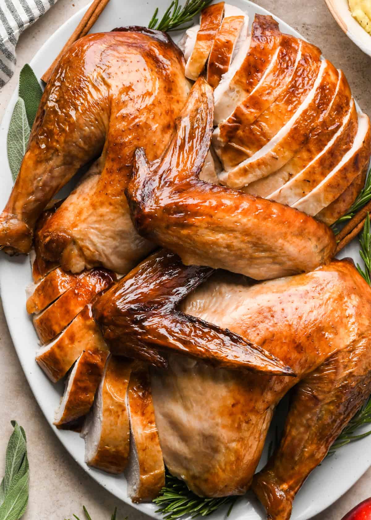 oven roast turkey carved into pieces like wings, thighs and sliced turkey breast on a serving plate with herbs