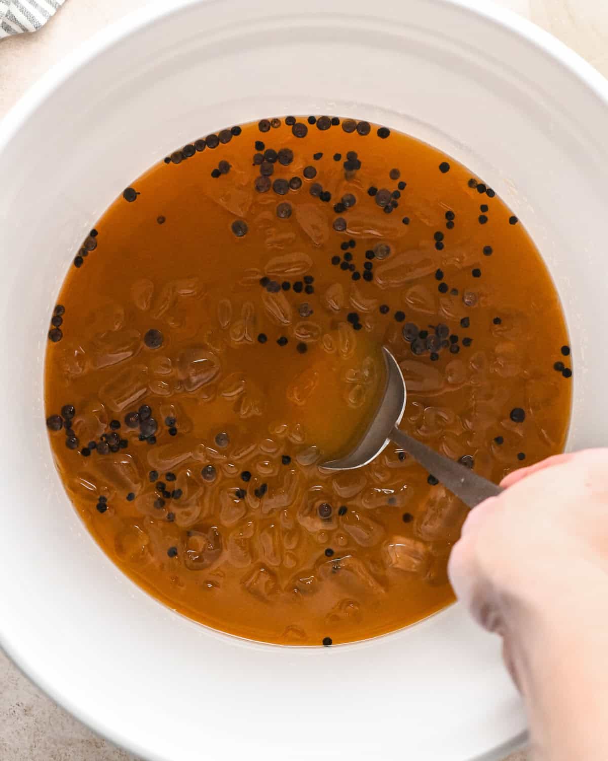 a metal spoon stirring turkey brine in a white bucket to make oven roasted turkey