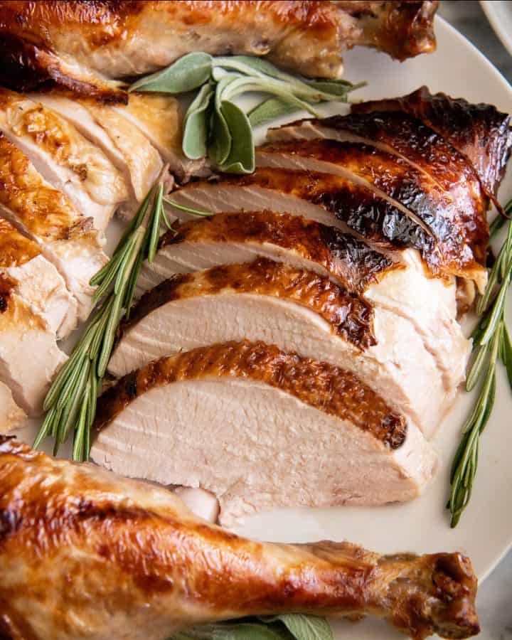 overhead view of roast turkey carved on a plate with herbs around it