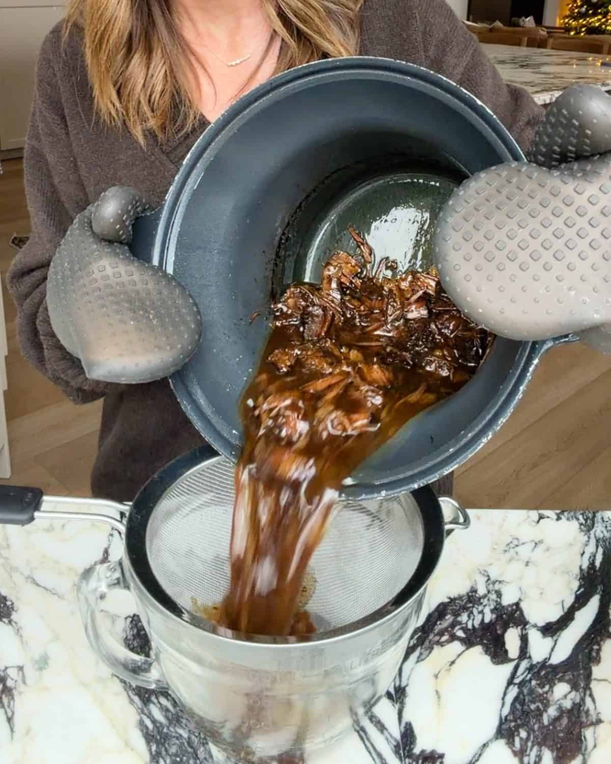 making slow cooker pot roast recipe - roast and liquid being poured through a fine mesh metal strainer into a glass batter bowl