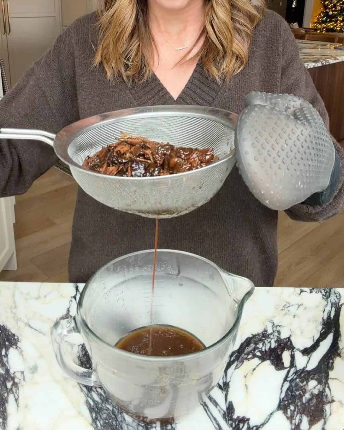 making slow cooker pot roast recipe - Laura from joyfoodsunshine holding up the fine mesh metal strainer to get out excess liquid over the glass batter bowl