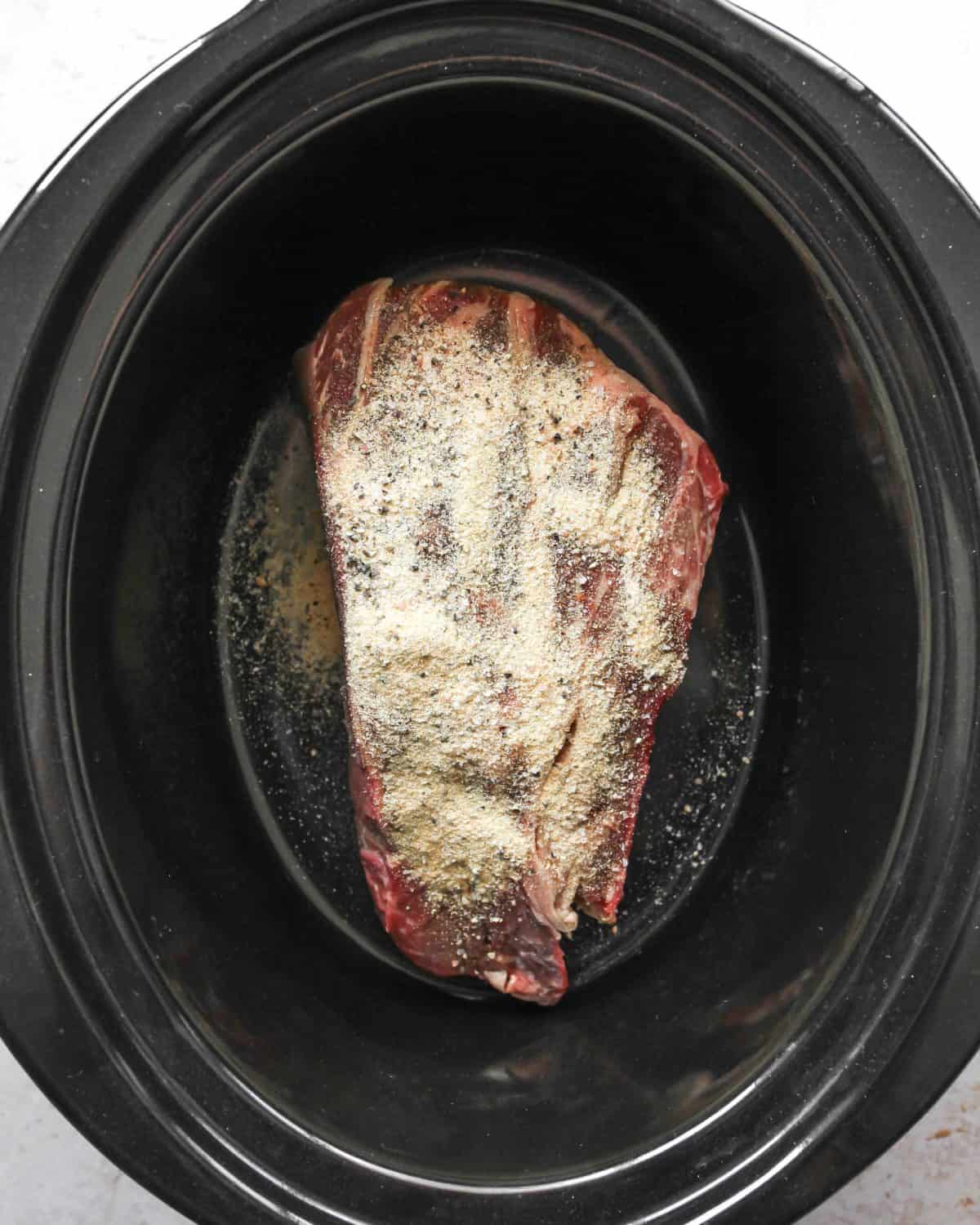 making slow cooker pot roast recipe - roast in a crock pot container covered in the spice rub and olive oil