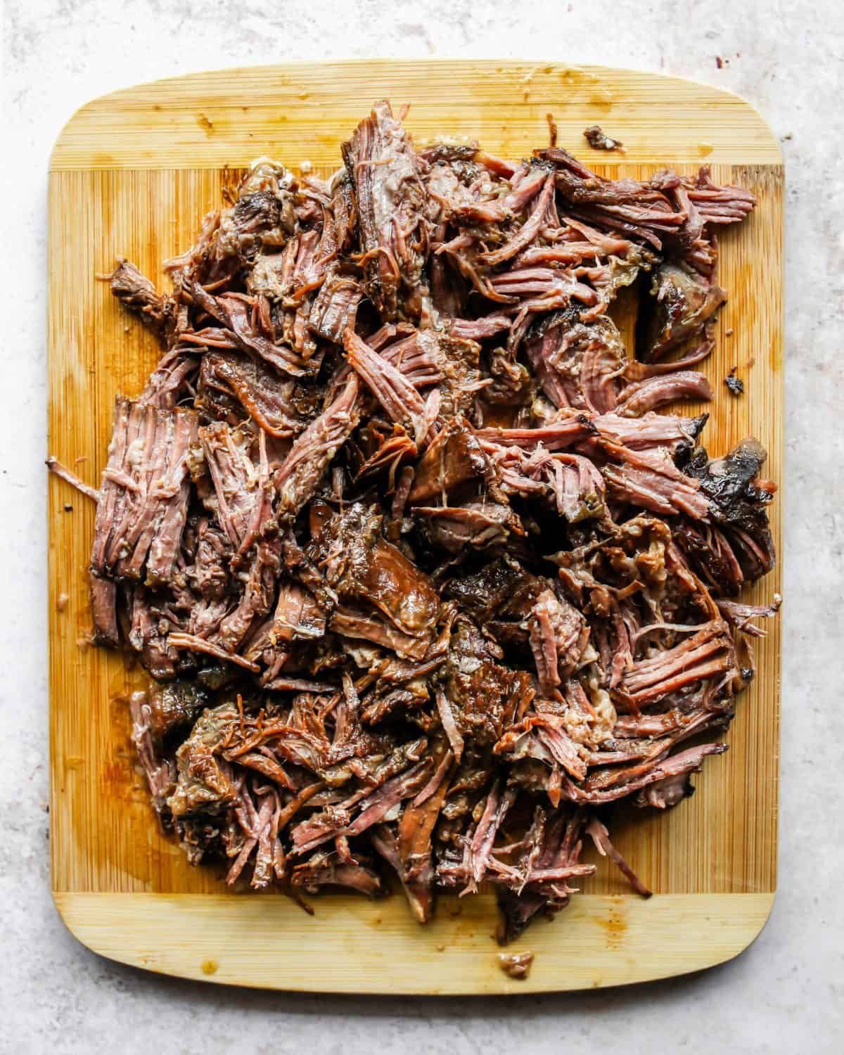 making slow cooker pot roast recipe - shredded pot roast on a wooden cutting board