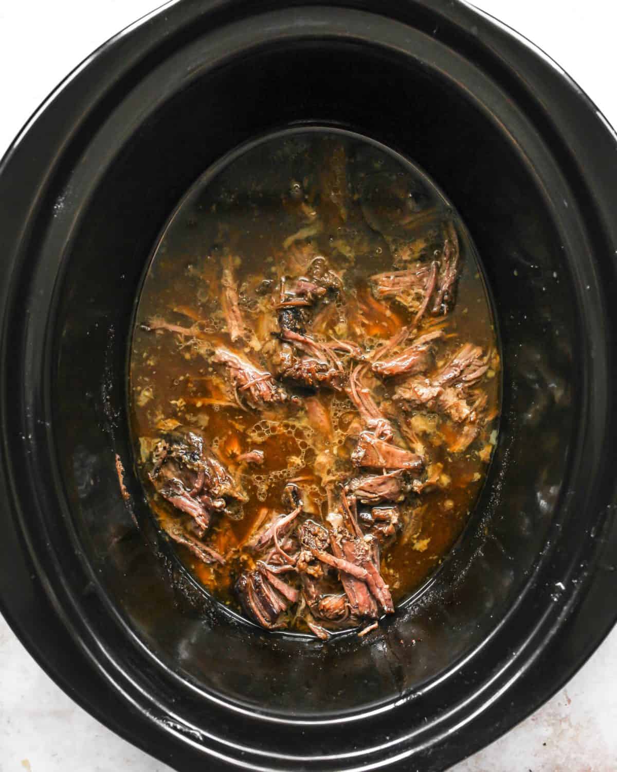 making slow cooker pot roast recipe - shredded meat in the crock pot with the sauce.