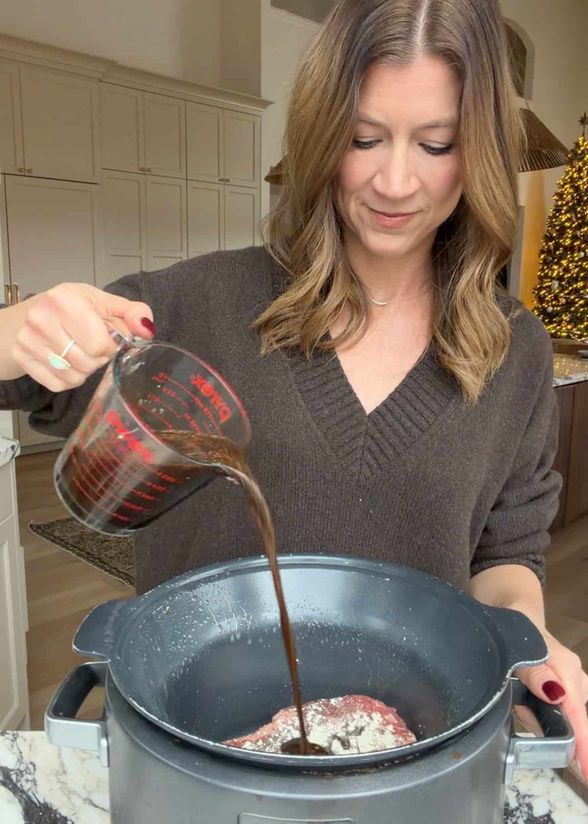 making slow cooker pot roast recipe - Laura from joyfoodsunshine pouring the sauce over the seasoned roasted in the crock pot