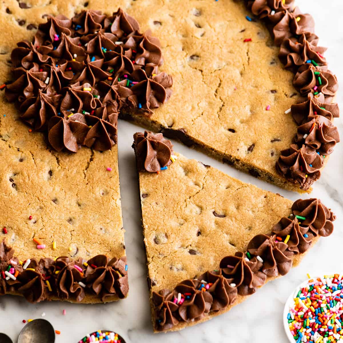 a chocolate chip cookie cake with chocolate frosting & sprinkles and one piece cut out of it