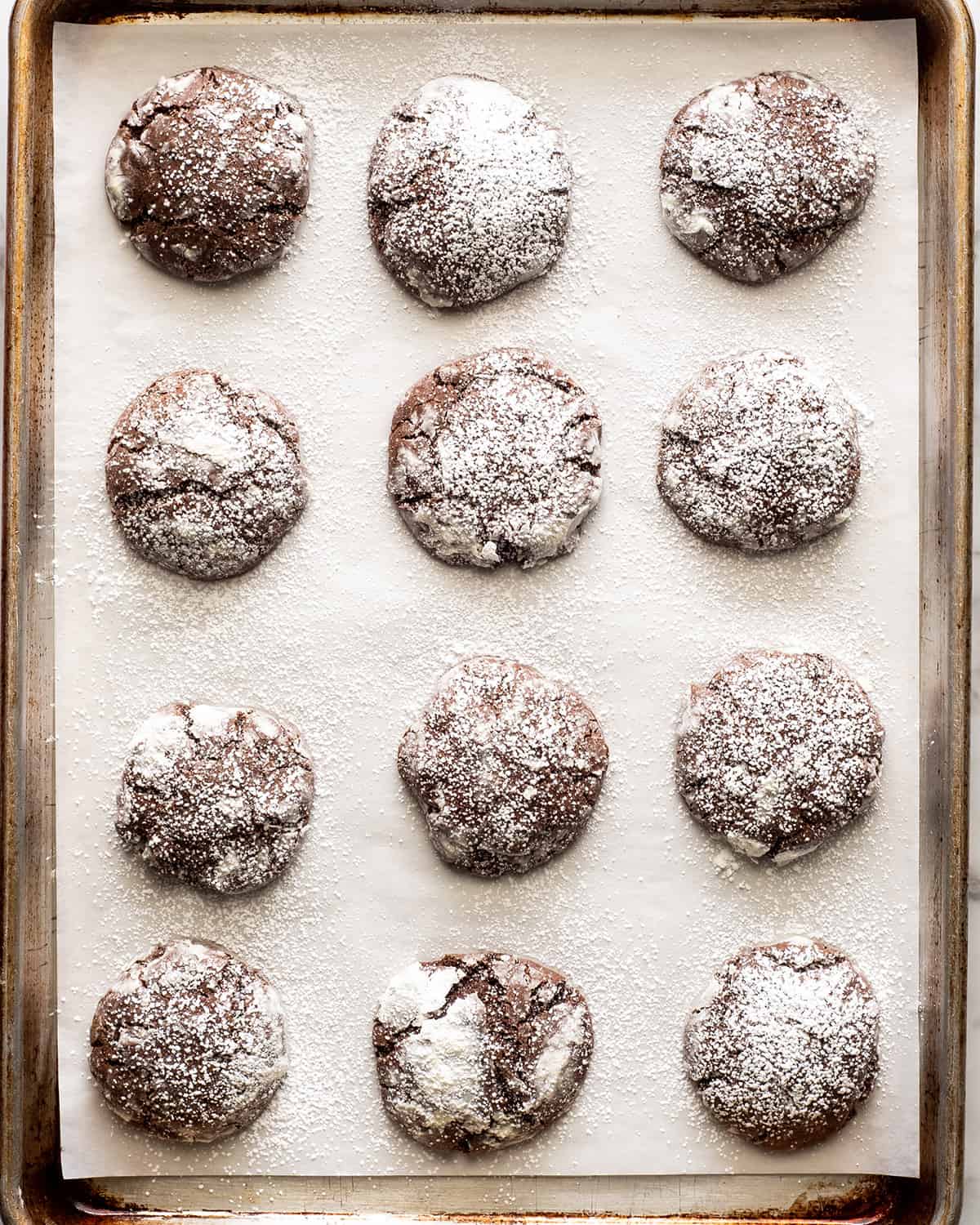 crinkles coated in powdered sugar on a baking sheet after baking