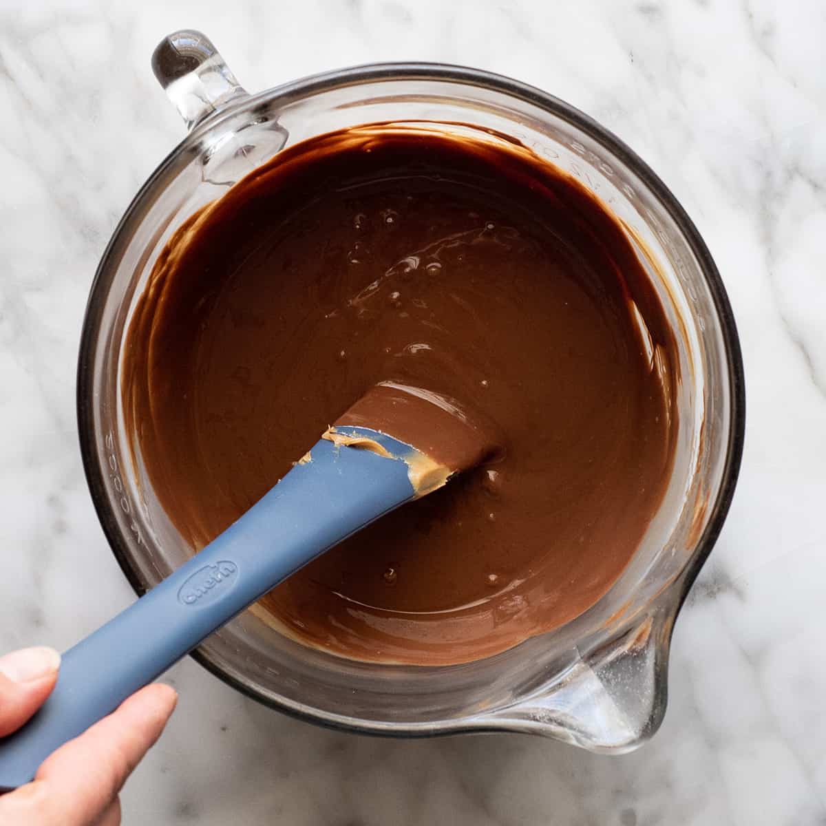 chocolate and peanut butter melted in a glass bowl with a spatula 