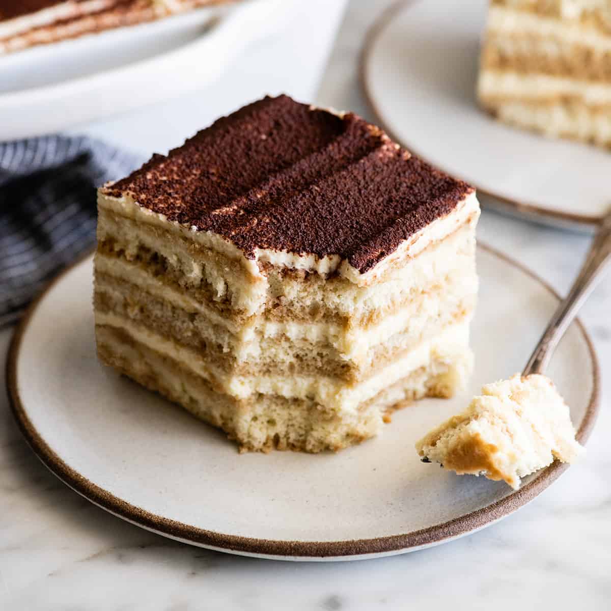 a piece of the Best Tiramisu on a plate with a bite taken out of it