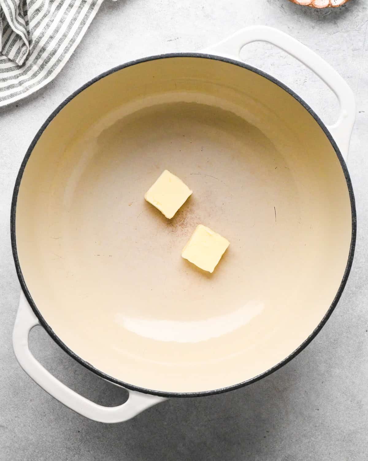 two square of butter in a white pot making homemade tomato soup, a striped towel is in the top left corner