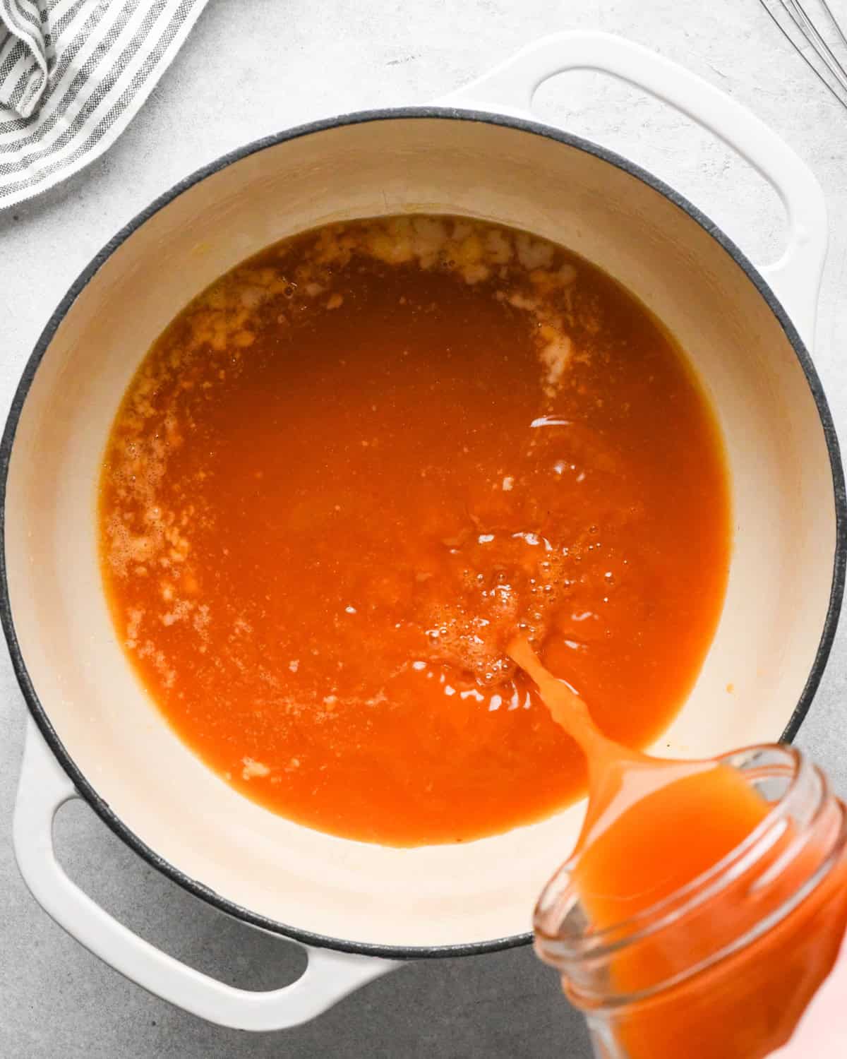 vegetable broth being poured into a butter/flour roux in a white pot to make tomato soup