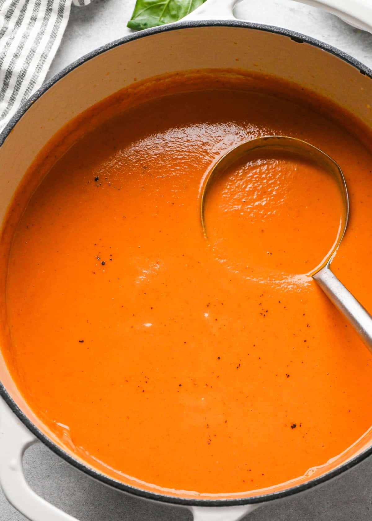 a pot of homemade tomato soup recipe garnished with cracked black pepper. There's a ladle in the soup taking a scoop. 