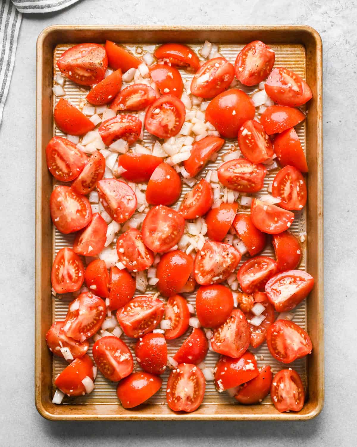 tomatoes, garlic, olive oil and onions spread out on a baking sheet before roasting to make this homemade tomato soup recipe