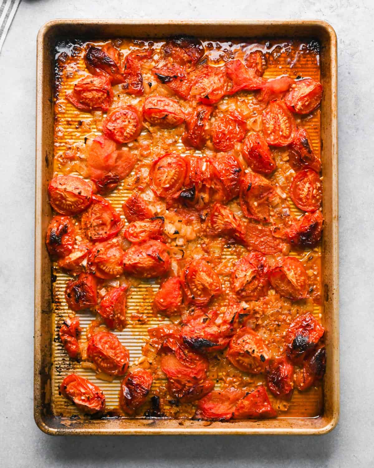 tomatoes, garlic, olive oil and onions being stirred with a wooden spoon on a baking sheet after roasting 