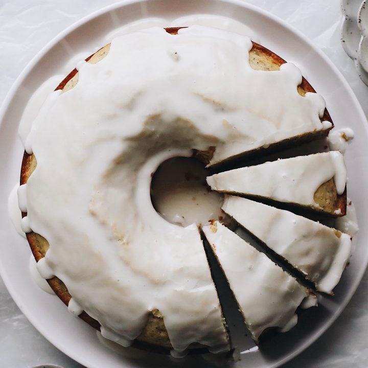 This poppy seed cake is moist, and sweet and easy to make in one bowl! It's an old, tried and tested recipe - and topped with a simple glaze - it is the best poppyseed cake ever. overhead photo of a Poppy Seed Cake on a serving plate with 3 slices cut