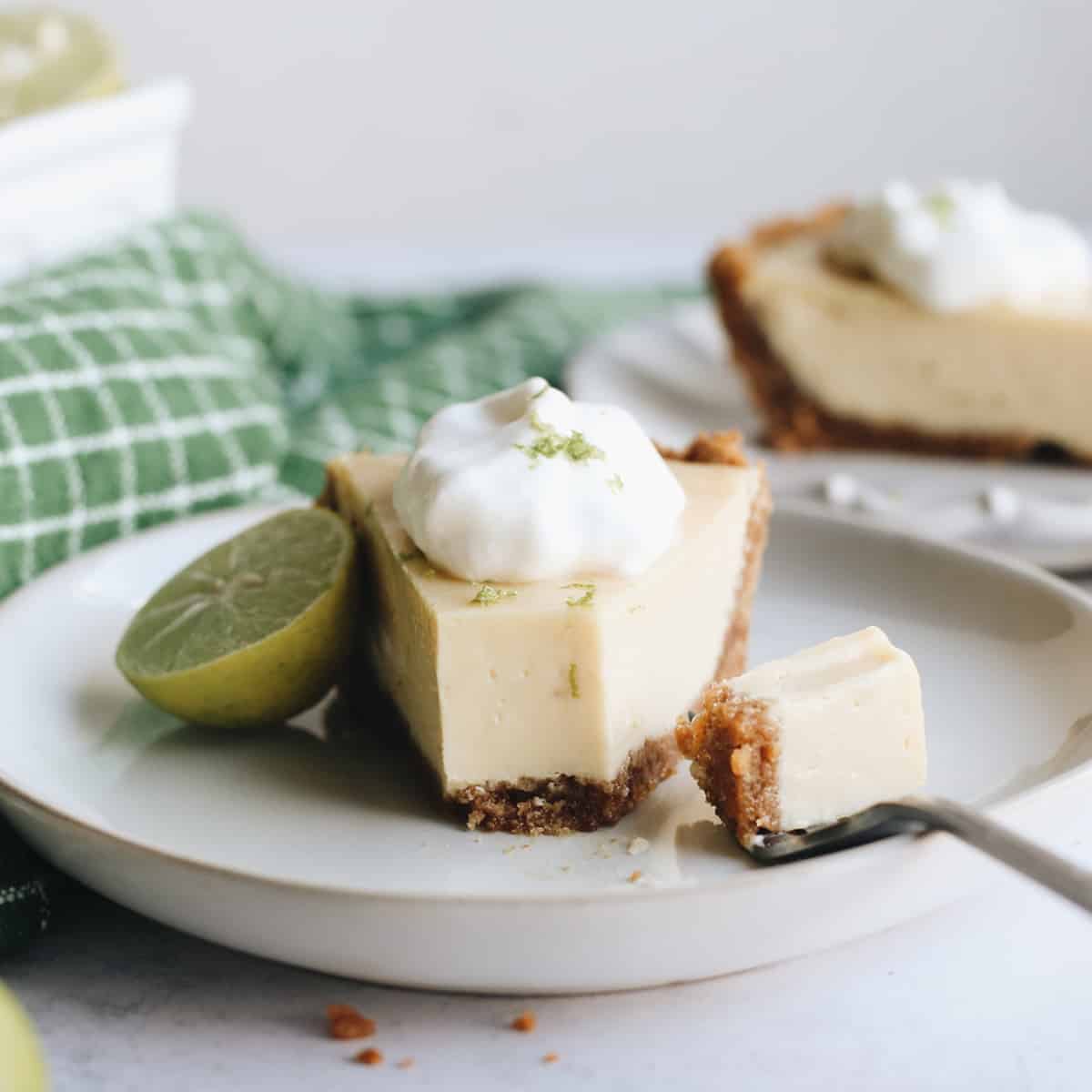 a piece of Key Lime Pie on a plate with whipped cream and one bite on a fork