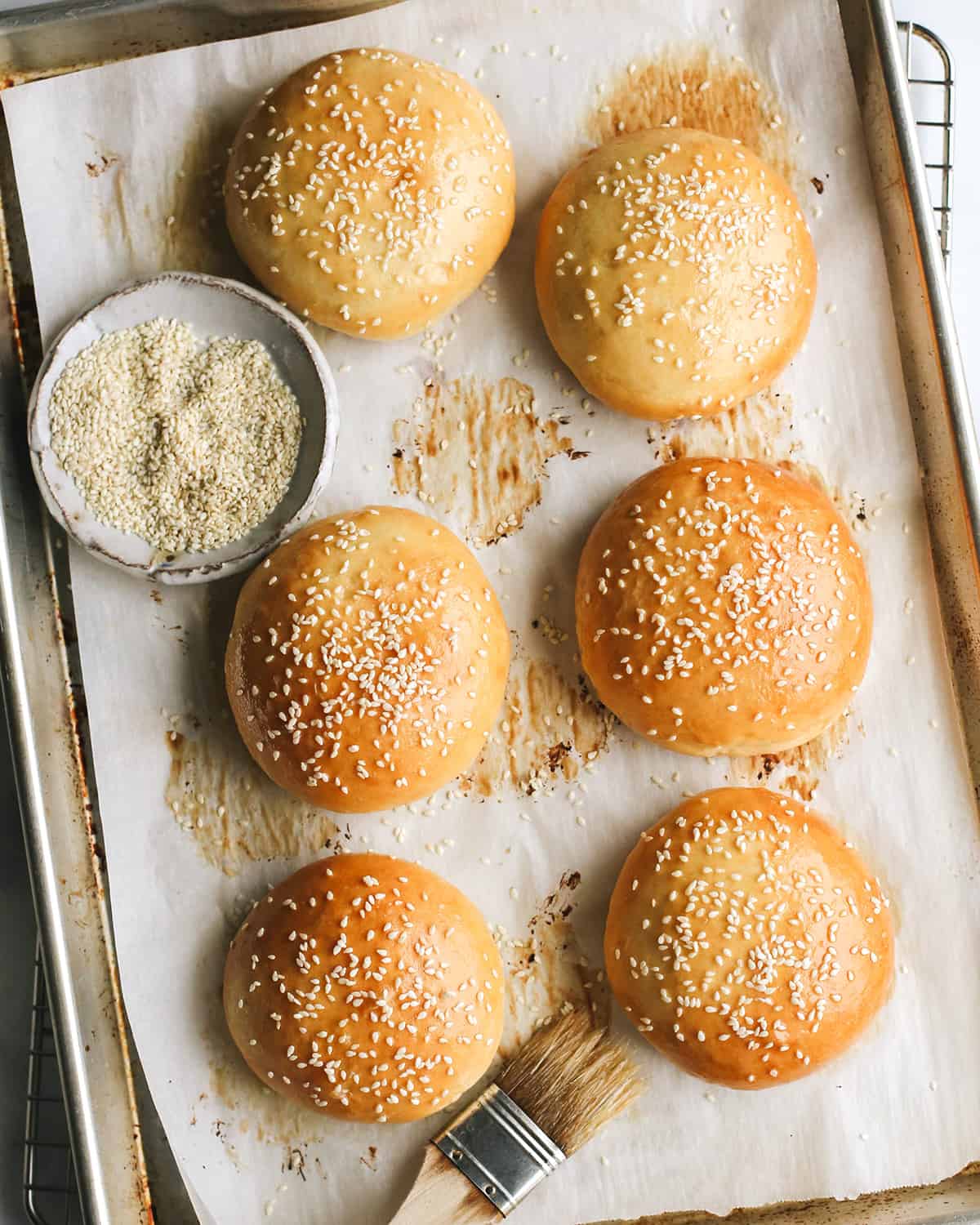 6 Homemade Hamburger Buns on a baking sheet after baking topped with sesame seeds 