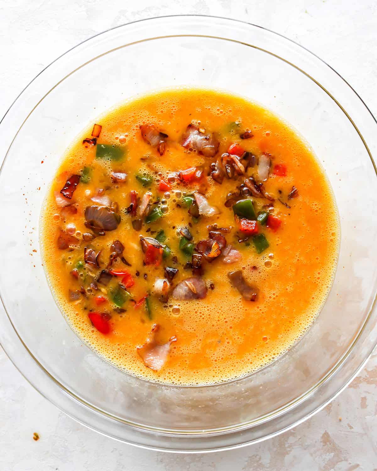 how to make egg bites - bacon and veggies added to the egg mixture in a glass bowl