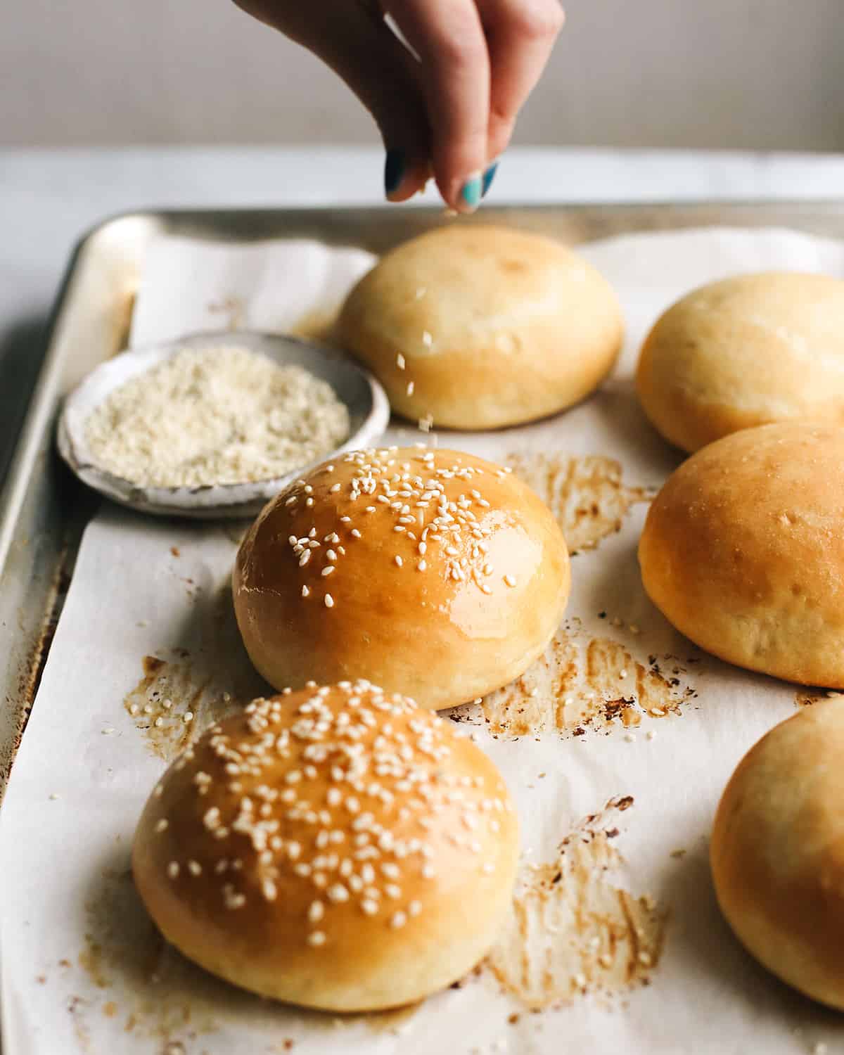 front view of sesame seeds being sprinkled on Homemade Burger Buns